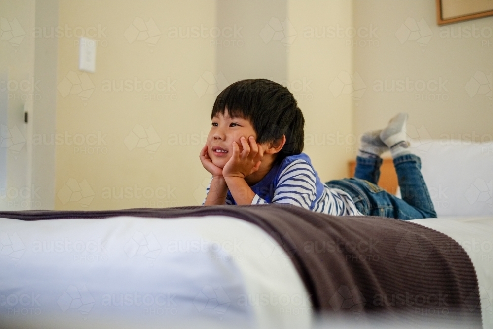 a kid lying on a bed watching tv - Australian Stock Image