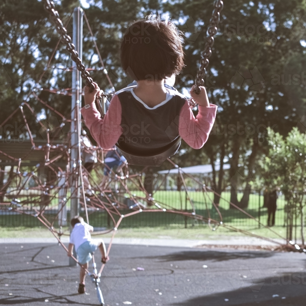 a kid riding a swing as the sun sets in spring - Australian Stock Image