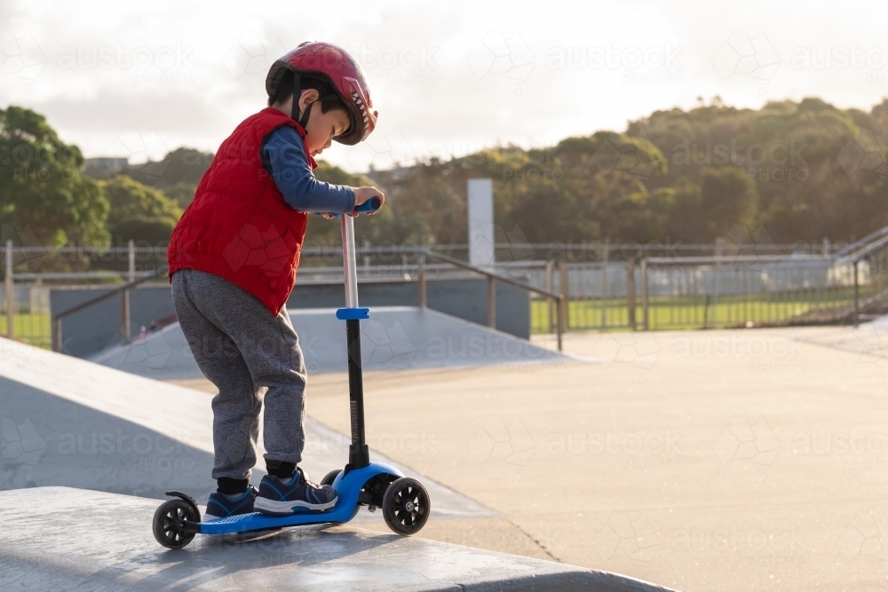 a kid riding his scooter on a ramp at a skate park - Australian Stock Image