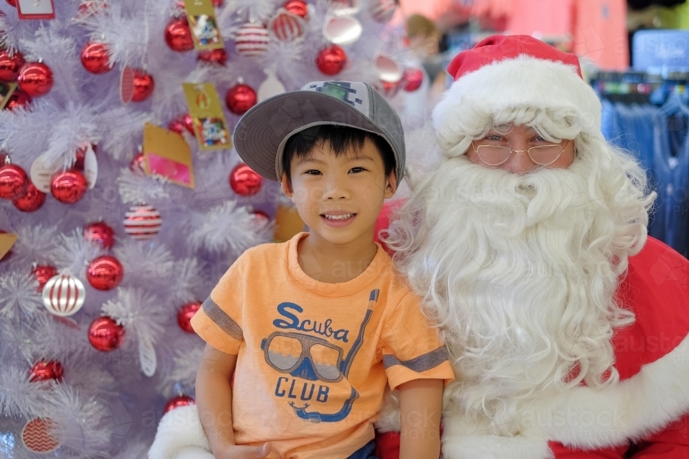 A kid, sitting on Santa's lap beside a Christmas tree - Australian Stock Image
