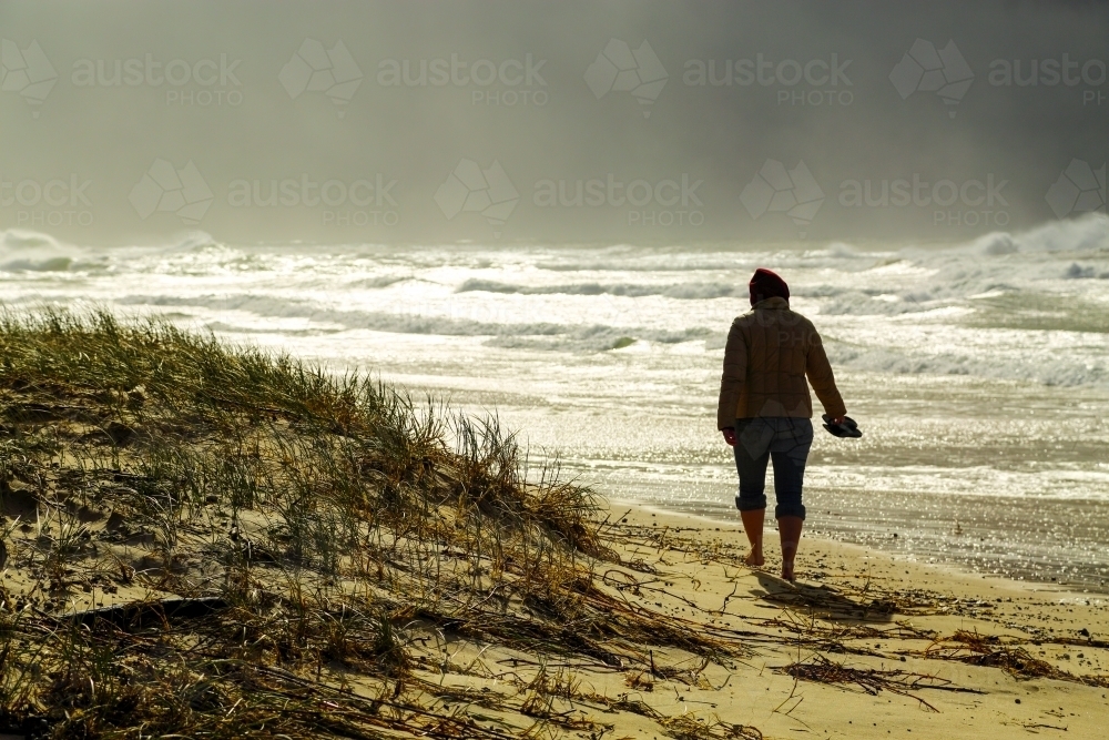 A lady in her mid thirties braves a storm as she strolls along a beach at Iluka, NSW - Australian Stock Image