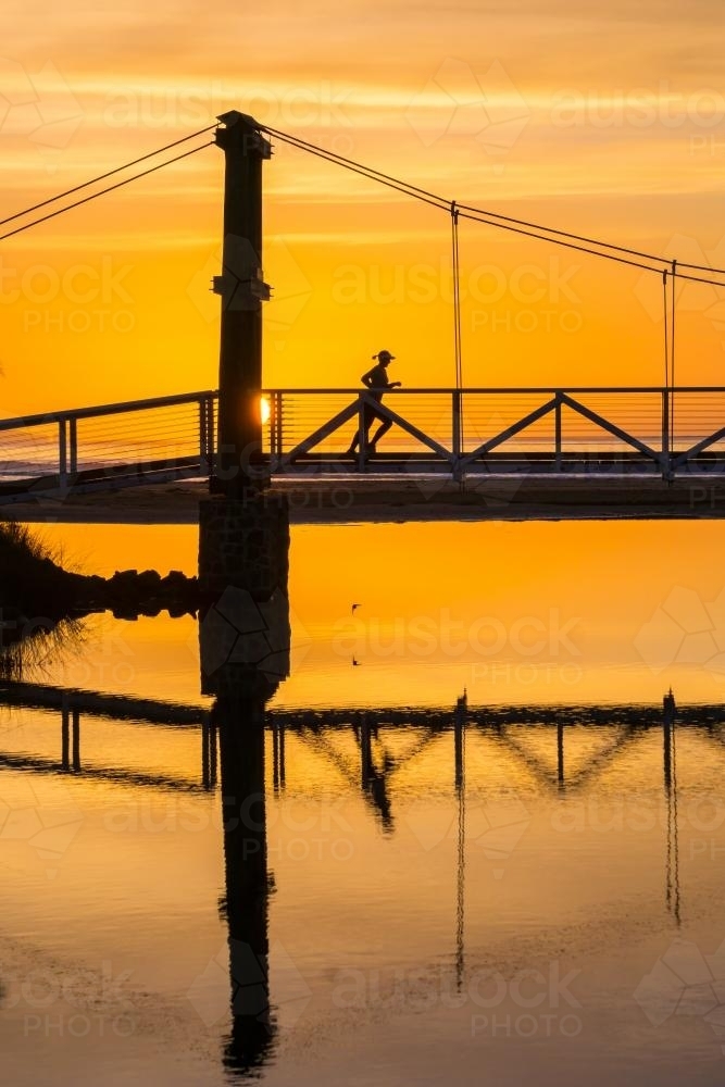 A lady runs across a footbridge at sunrise - Australian Stock Image