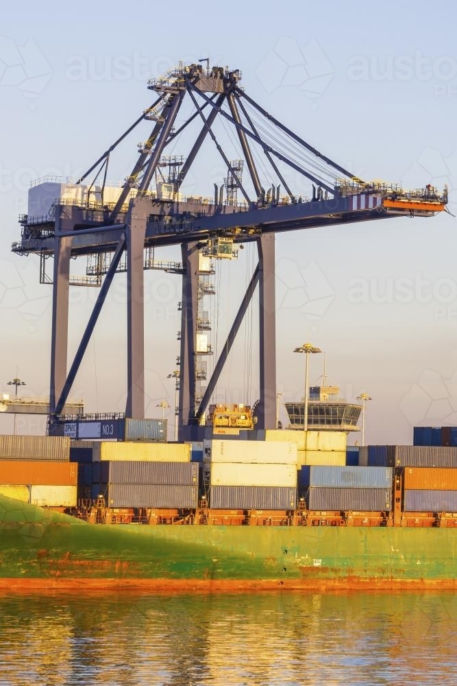 A large crane loading containers on to a ship at a dock - Australian Stock Image