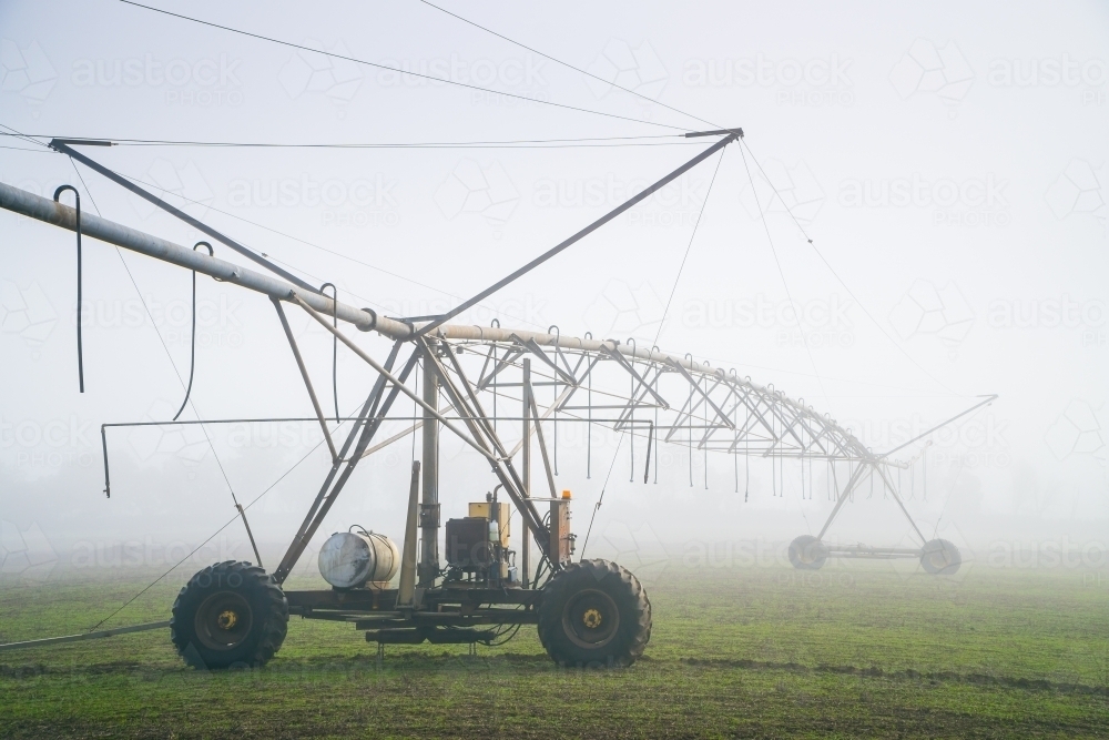 A large irrigation sprinkler in a paddock on a foggy morning - Australian Stock Image