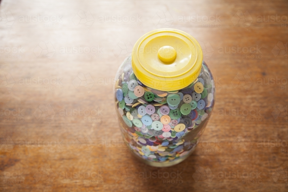 A Large jar of buttons sitting on a wooden table - Australian Stock Image