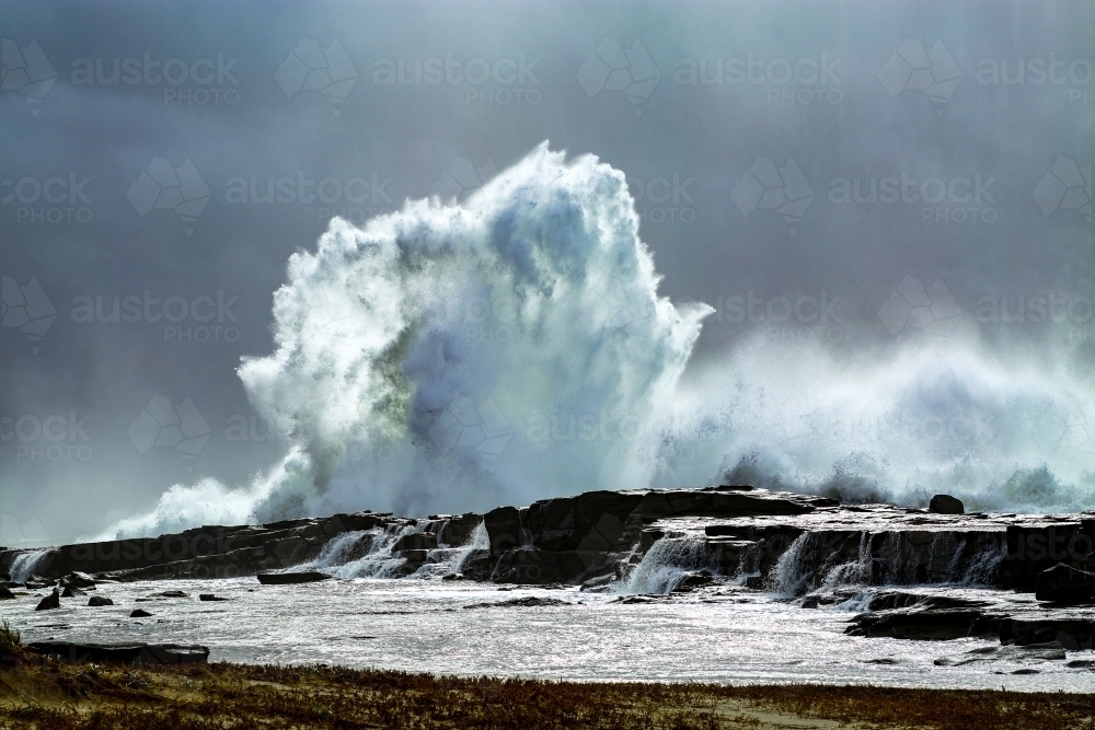 A large swell smashes against a rocky headland under a stormy sky in Iluka, New South Wales - Australian Stock Image