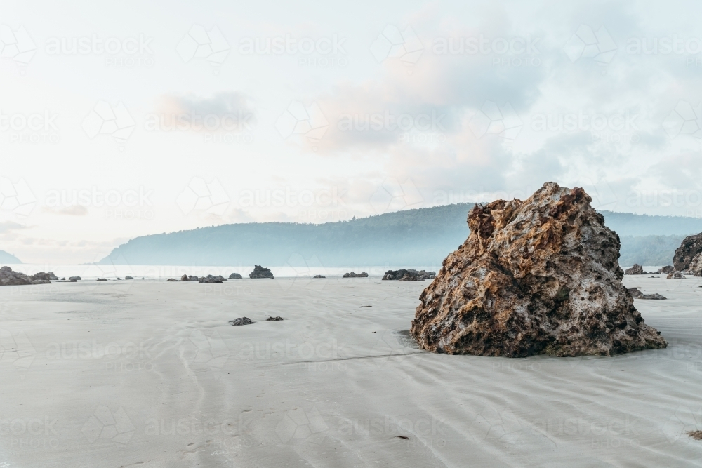 A large, textured rock formation stands on a sandy beach. - Australian Stock Image