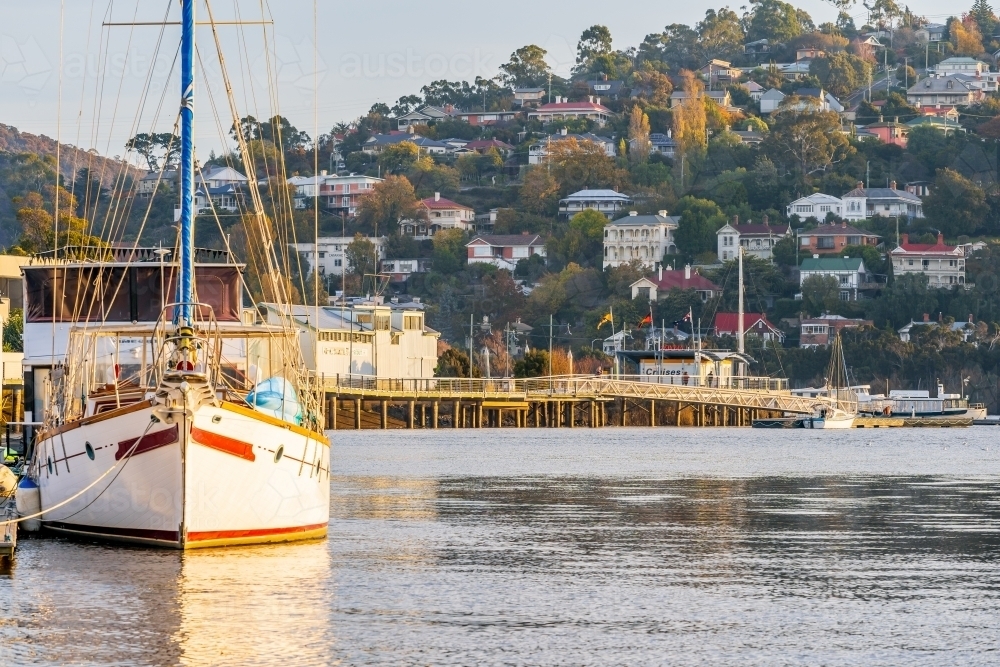 A large yacht docked at a jetty on a calm river in late afternoon sunshine - Australian Stock Image