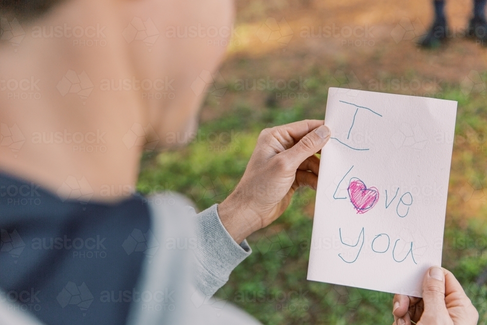 A letter with an I love you text and a red heart written on a small paper held by a man in blur - Australian Stock Image