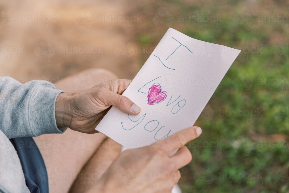 A letter with an I love you text and a red heart written on a small paper held by a man in two hands - Australian Stock Image