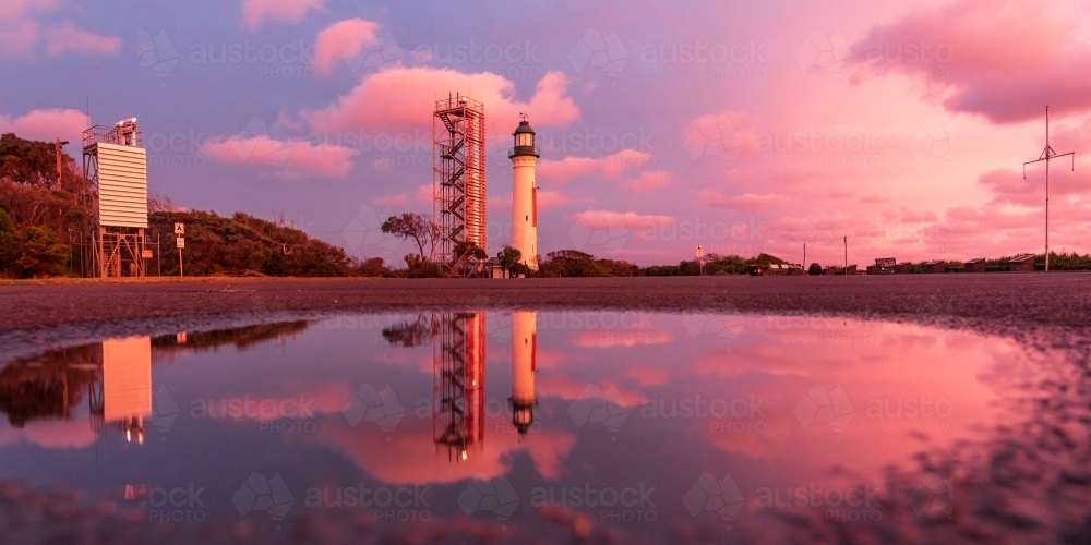 A lighthouse and its reflection against a colourful sunset sky - Australian Stock Image