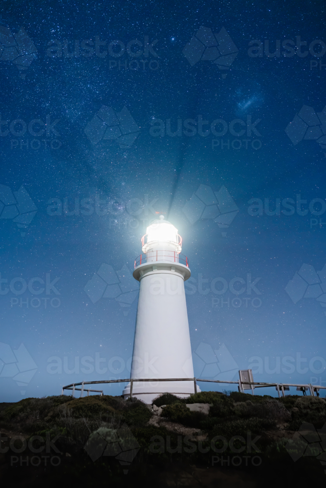 A lighthouse stands illuminated beneath a vast, star‑filled sky - Australian Stock Image