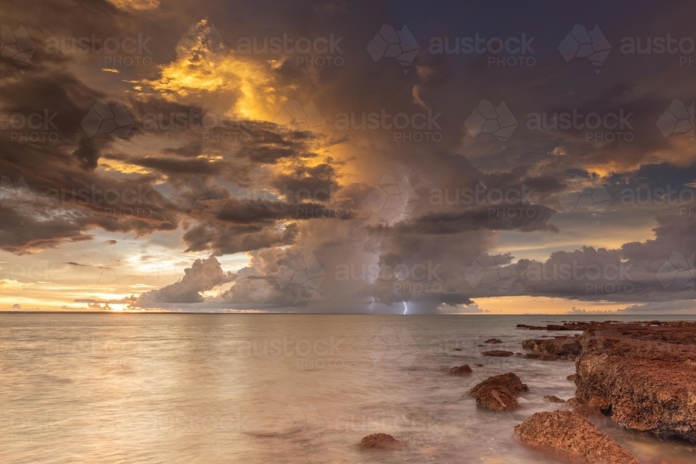 A lightning storm in the distance over the ocean during sunset - Australian Stock Image