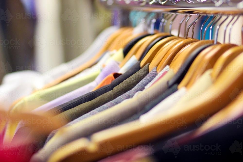 A line of shirts hanging on coat hangers in a second hand store - Australian Stock Image