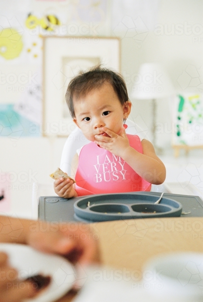 A little girl toddler eating a healthy meal on a highchair - Australian Stock Image
