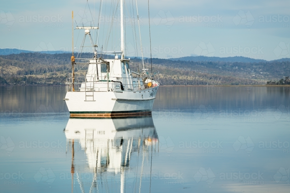 A lone yacht reflected in the calm waters of a river - Australian Stock Image