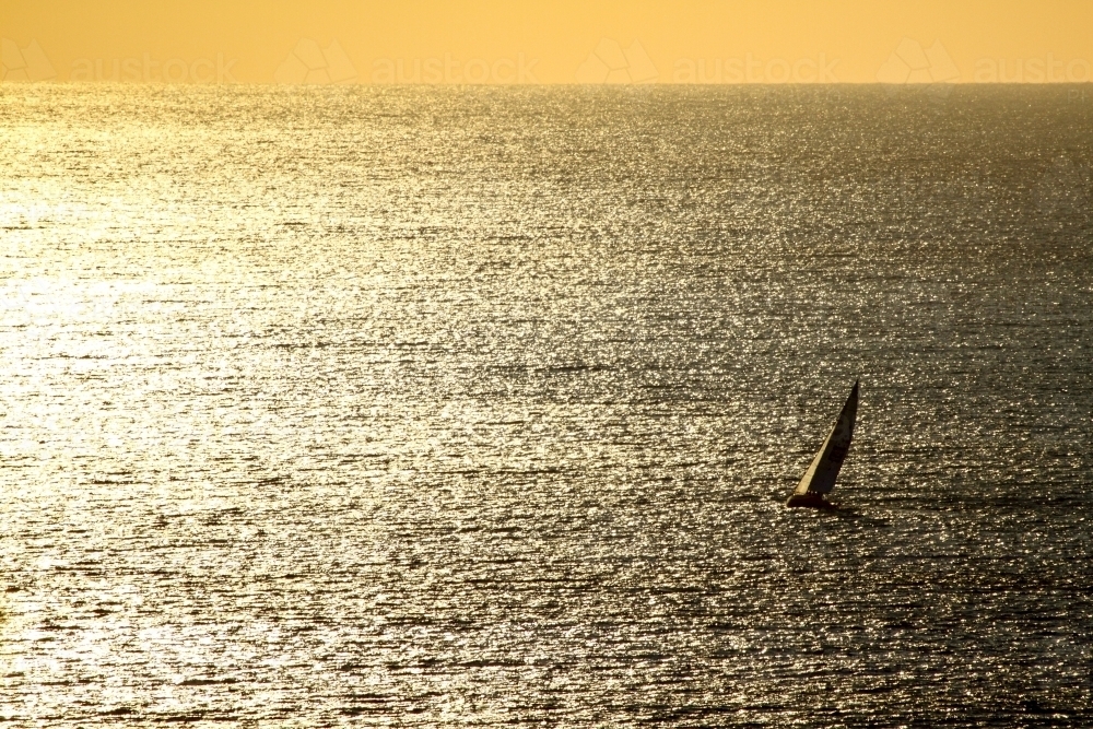 A lone yacht sailing on a vast shimmering ocean at sunrise - Australian Stock Image