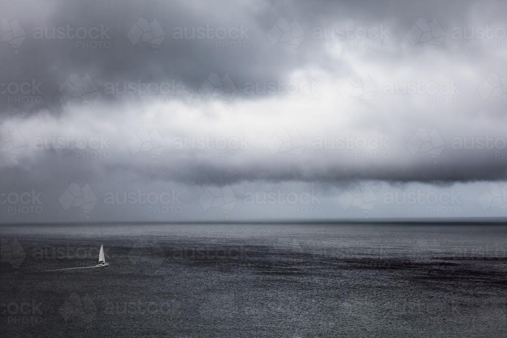 A lone yacht sailing the ocean under stormy grey skies - Australian Stock Image