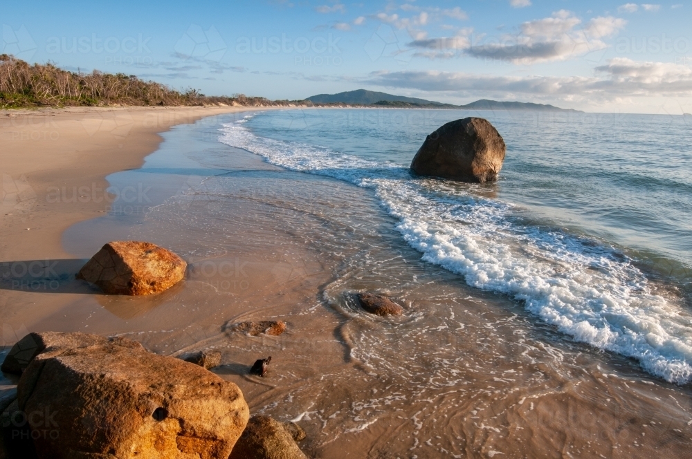A long beach with boulders in the foreground taken around sunrise - Australian Stock Image