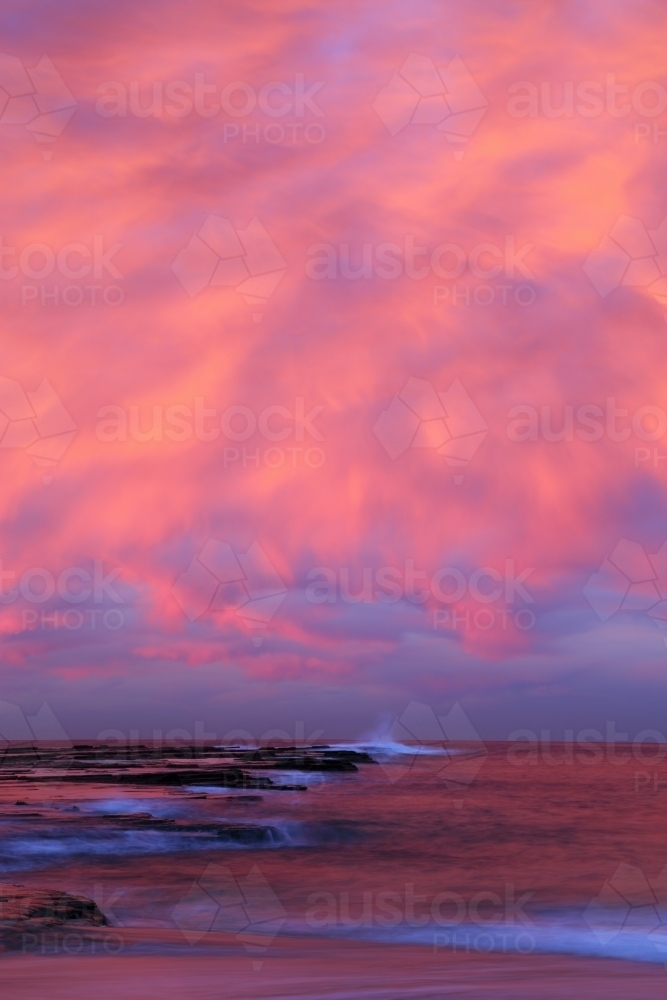 A long exposure of dramatic pink cloudy sunset over the beach and ocean at Coledale, Illawarra, NSW - Australian Stock Image