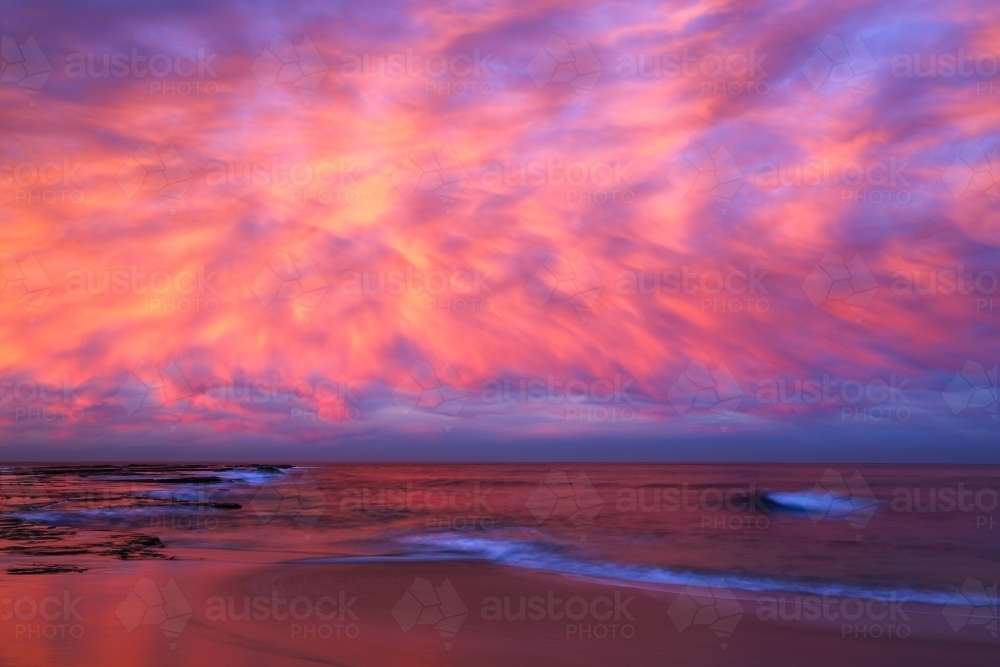 A long exposure of dramatic pink cloudy sunset over the beach and ocean at Coledale, Illawarra, NSW - Australian Stock Image