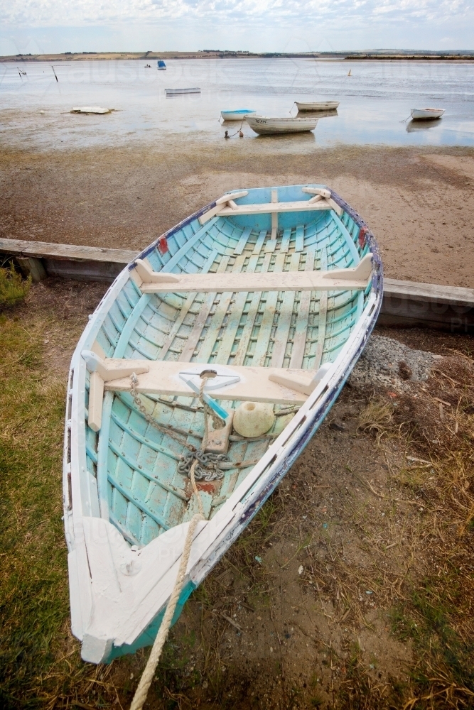 A long narrow rowboat pulled ashore on the edge of shallow bay - Australian Stock Image