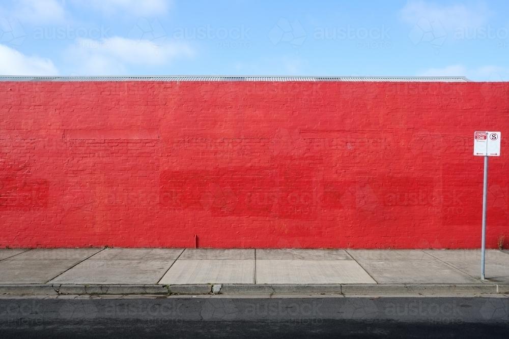 A long red wall with a street sign in front of it - Australian Stock Image