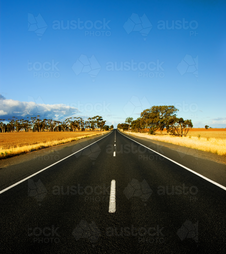 A long, straight country road stretches toward the horizon beneath a vivid blue sky - Australian Stock Image