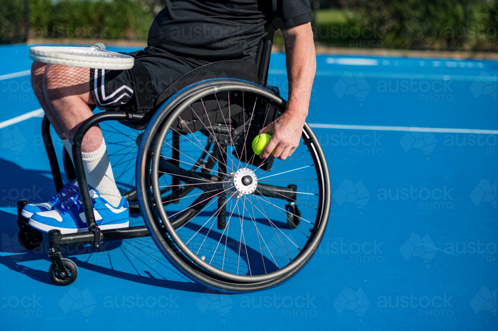 A male athlete in a wheelchair getting a tennis ball from the wheelchair - Australian Stock Image