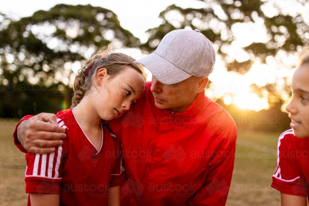A male football coach with his arm around a player encouraging her - Australian Stock Image