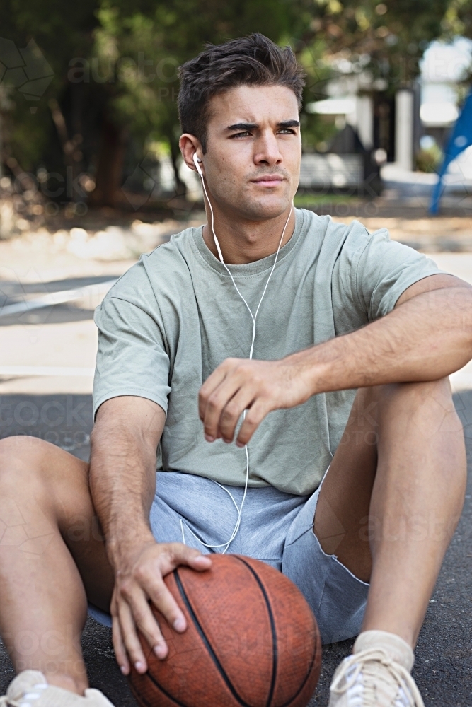 A male in his twenties holding a basketball / taking a break on an outdoor basketball court - Australian Stock Image