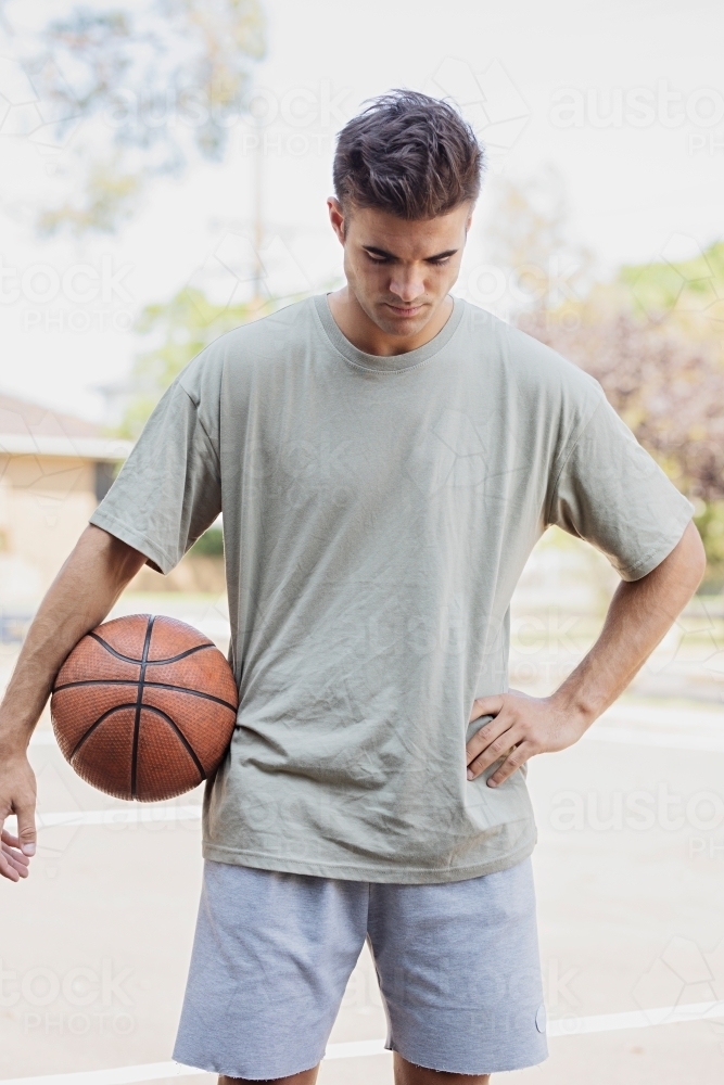 A male in his twenties holding a basketball / taking a break on an outdoor basketball court - Australian Stock Image