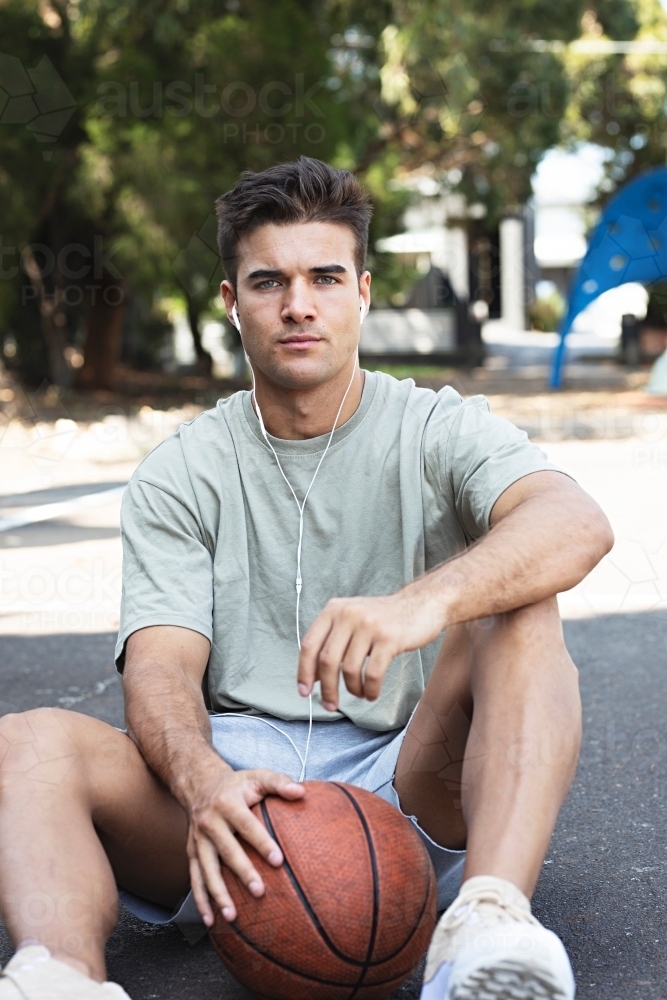 A male in his twenties holding a basketball / taking a break on an outdoor basketball court - Australian Stock Image
