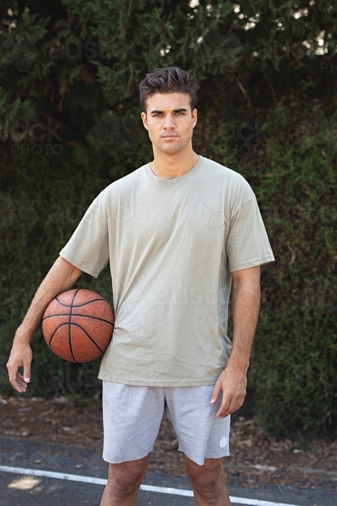 A male in his twenties holding a basketball / taking a break on an outdoor basketball court - Australian Stock Image
