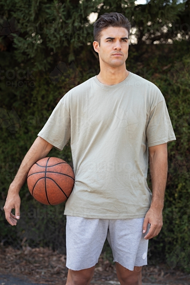 A male in his twenties holding a basketball / taking a break on an outdoor basketball court - Australian Stock Image