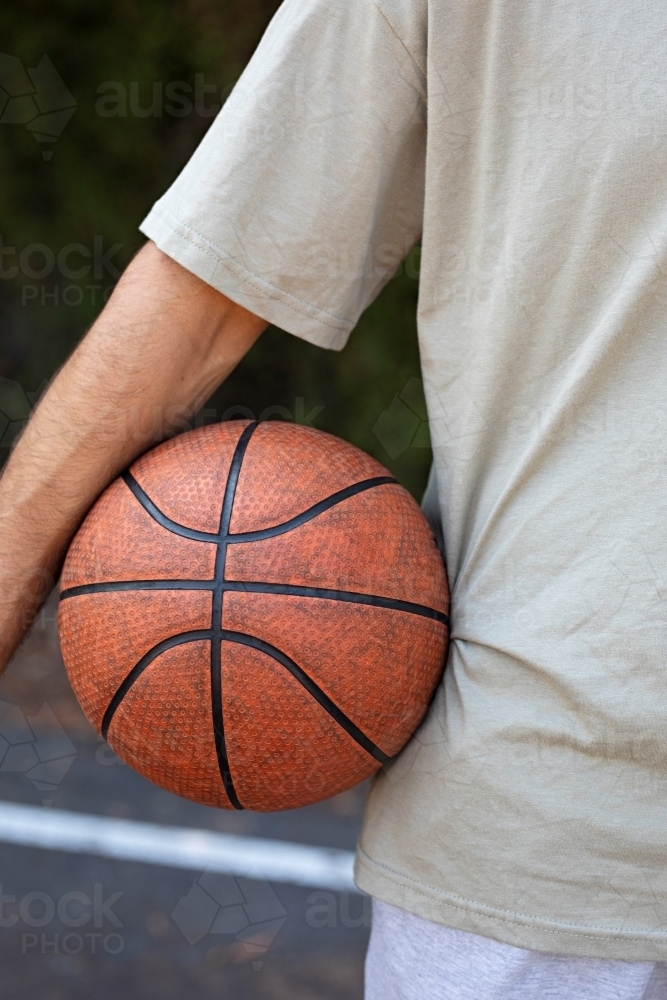 A male in his twenties holding a basketball / taking a break on an outdoor basketball court - Australian Stock Image