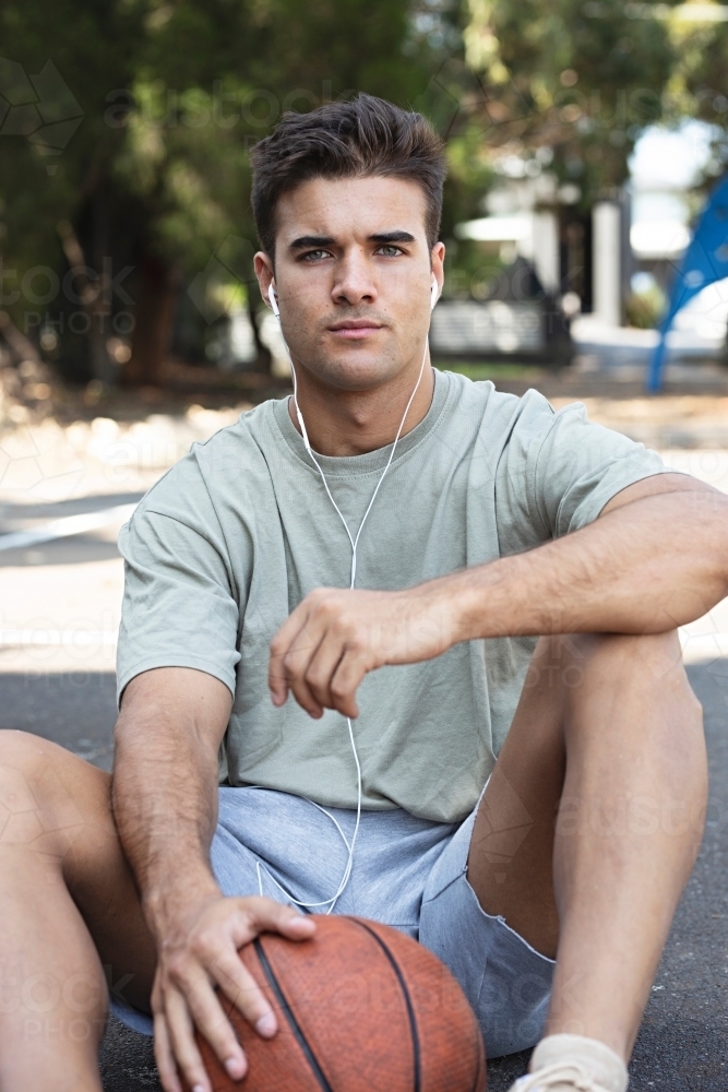 A male in his twenties holding a basketball / taking a break on an outdoor basketball court - Australian Stock Image