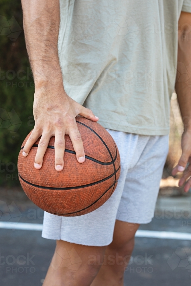 A male in his twenties holding a basketball / taking a break on an outdoor basketball court - Australian Stock Image