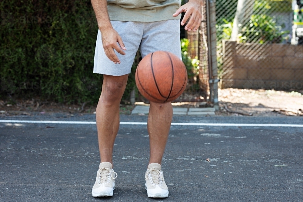 A male in his twenties with a basketball / taking a break on an outdoor basketball court - Australian Stock Image