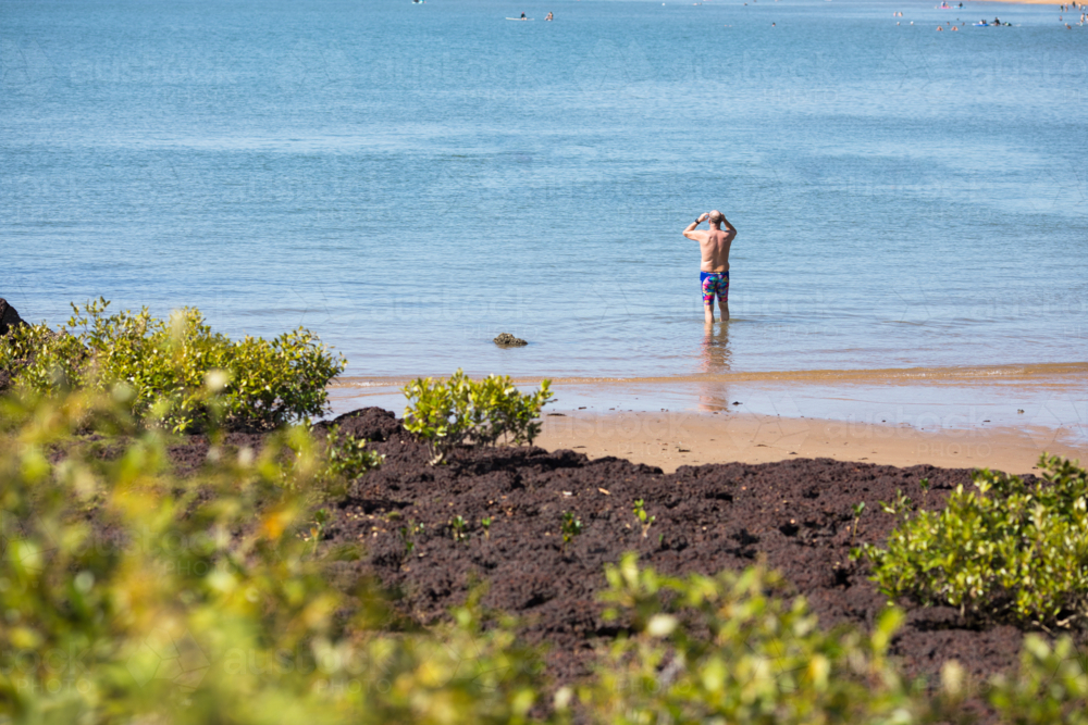 A male middle aged open water swimmer standing in the water at Suttons Beach, Redcliffe - Australian Stock Image