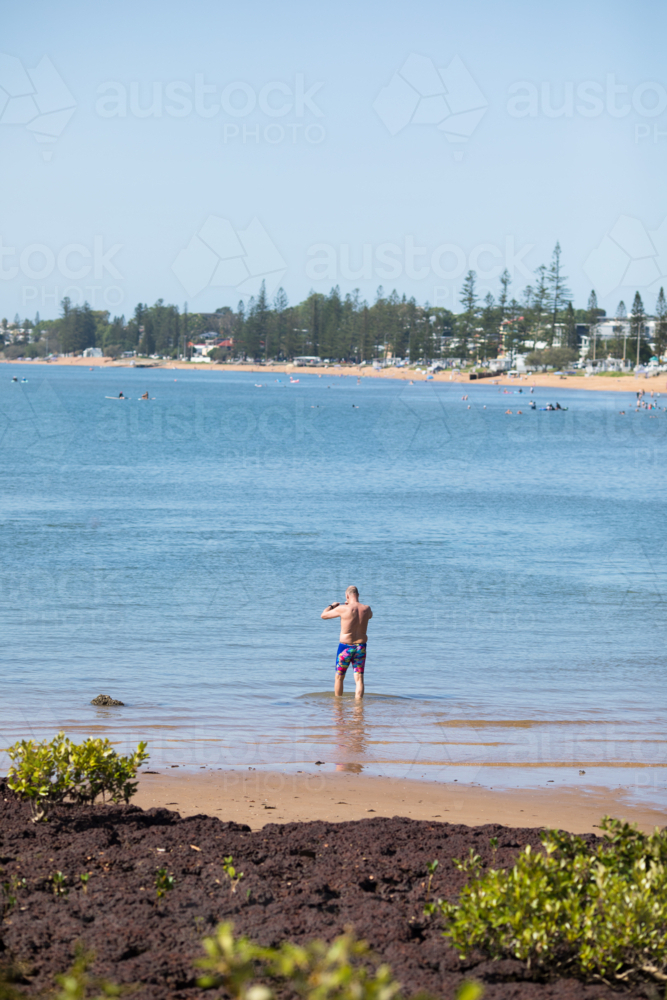 A male middle aged open water swimmer standing in water at Suttons Beach, Redcliffe - Australian Stock Image