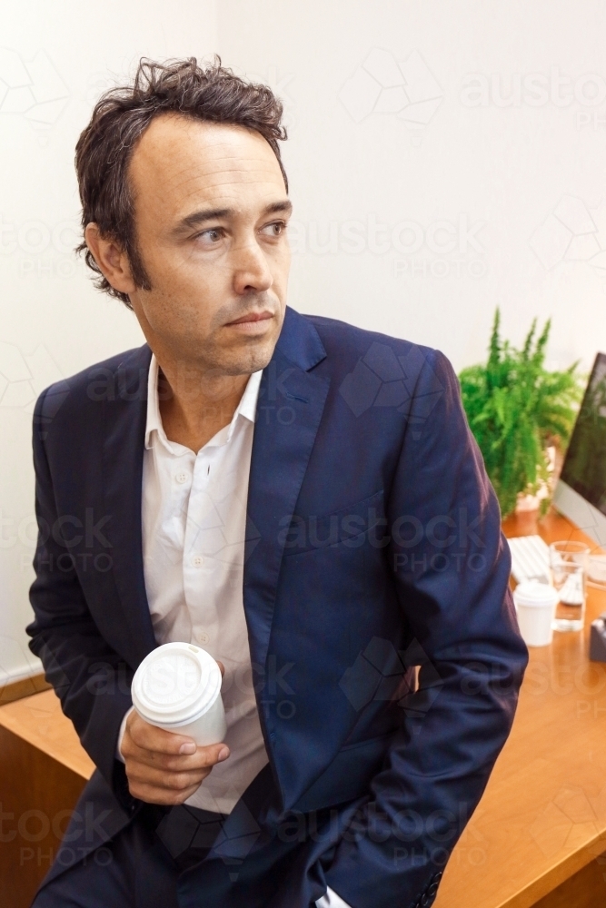 A male office worker leaning on work desk deep in thought - Australian Stock Image