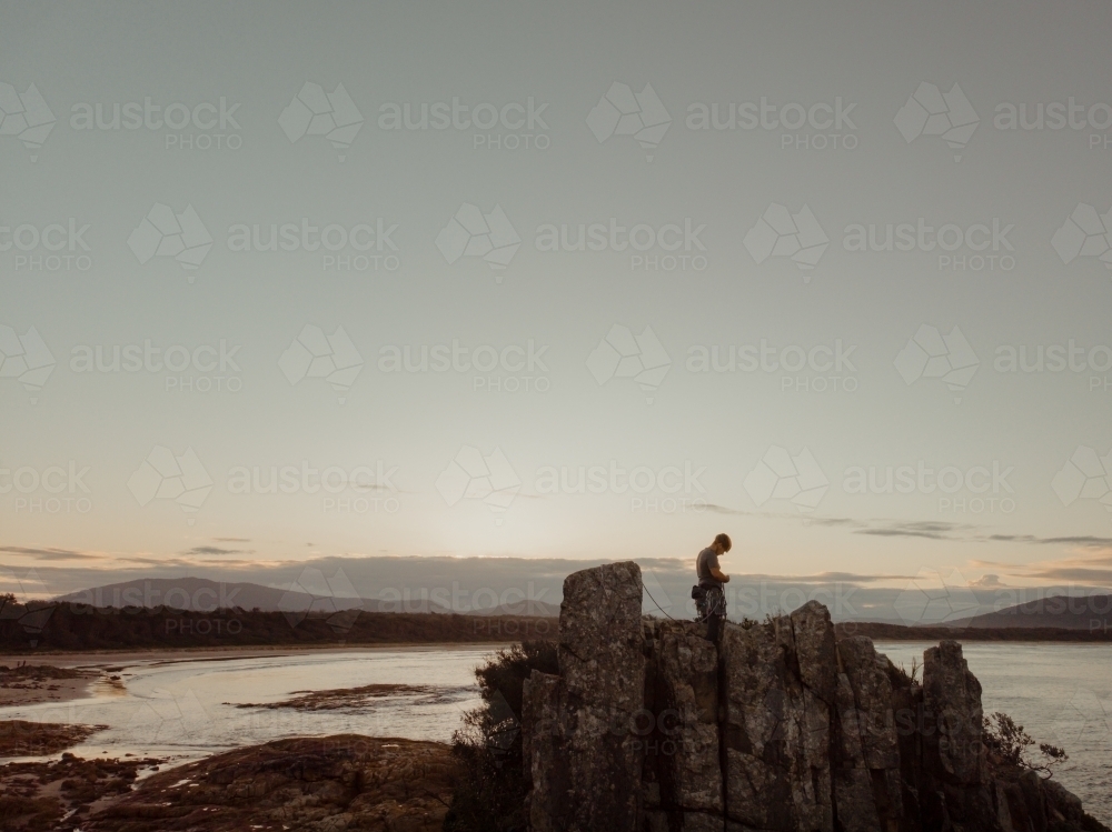 A male rock climber at the summit of a climbing route at sunset. - Australian Stock Image