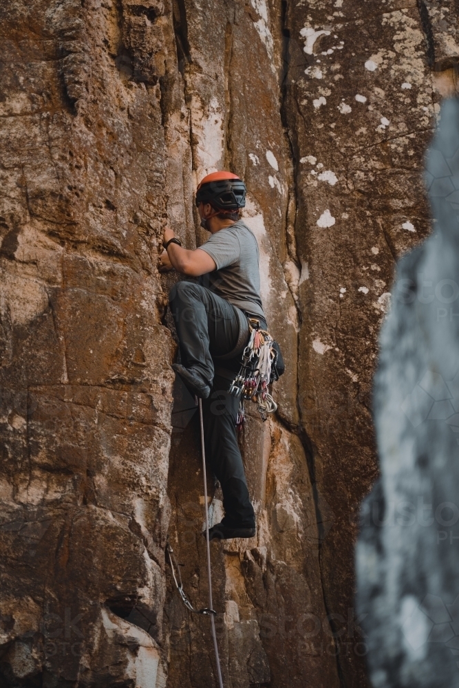 A male rock climber placing 'trad' gear into a cliff for a climbing route at Diamond Beach. : Austockphoto A male rock climber placing 'trad' gear into a cliff for a climbing route at Diamond Beach. - Australian Stock Image