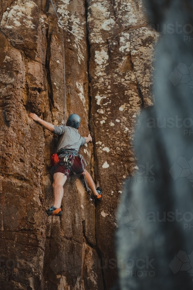 A male rock climber reaching for a hold on a climbing route at Diamond Beach. - Australian Stock Image
