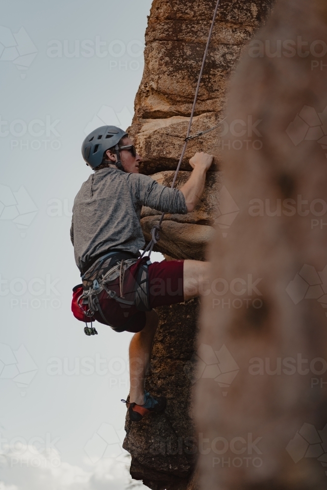 A male rock climber tackling a climbing route at Diamond Beach. : Austockphoto A male rock climber tackling a climbing route at Diamond Beach. - Australian Stock Image