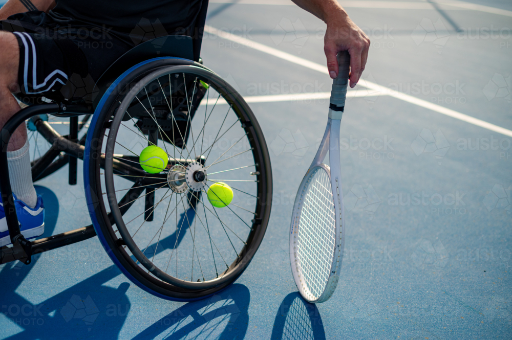 A male wheelchair tennis player is ready, holding a racquet near tennis balls on the court. - Australian Stock Image