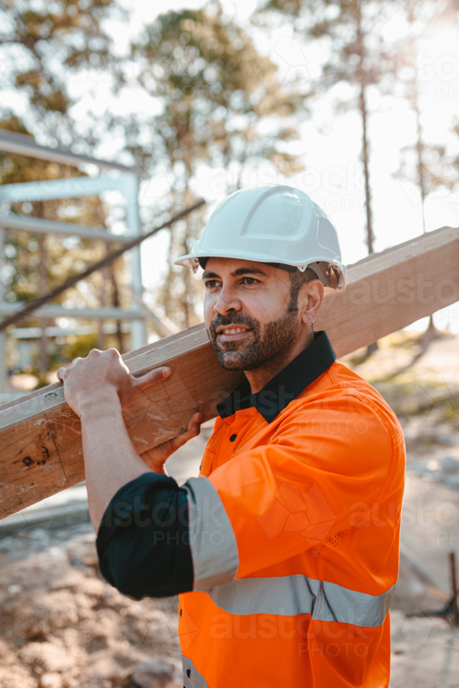 A man carrying a piece of lumber on his shoulder at a construction site - Australian Stock Image