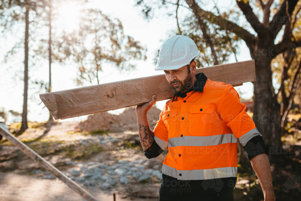 A man carrying a piece of wood on his shoulder at a construction site - Australian Stock Image