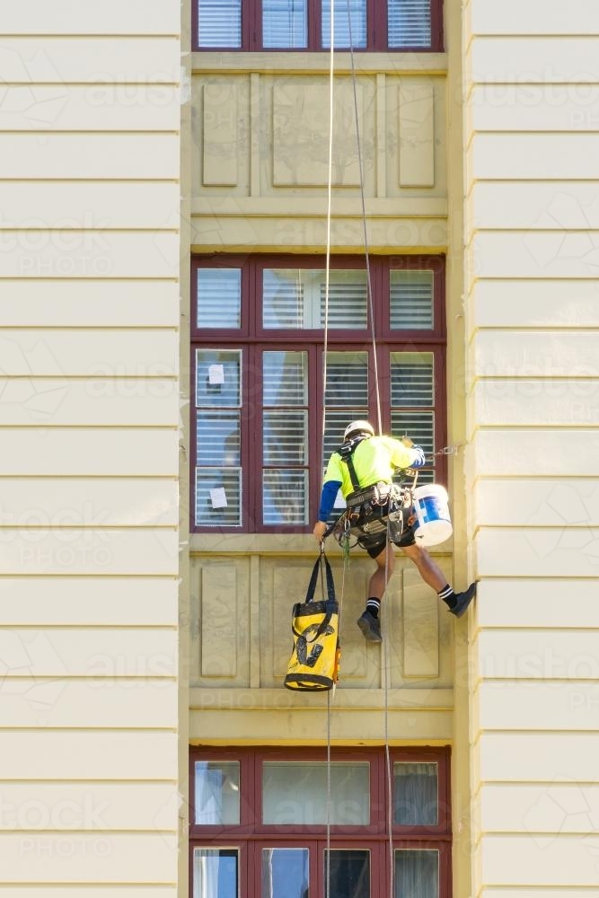 A man fixing windows, dangling down the side of a building - Australian Stock Image